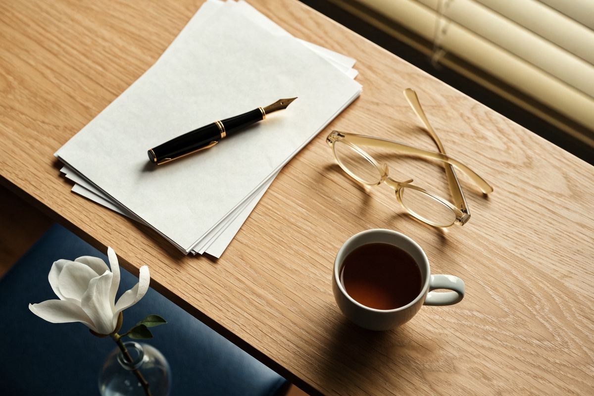 A magnolia blossom, fountain pen and cup of tea on a light oak desk